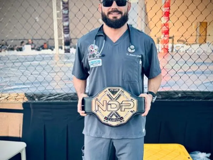 El Dr. Grimaldo en pijama quirúrgica junto a la jaula en un evento de MMA